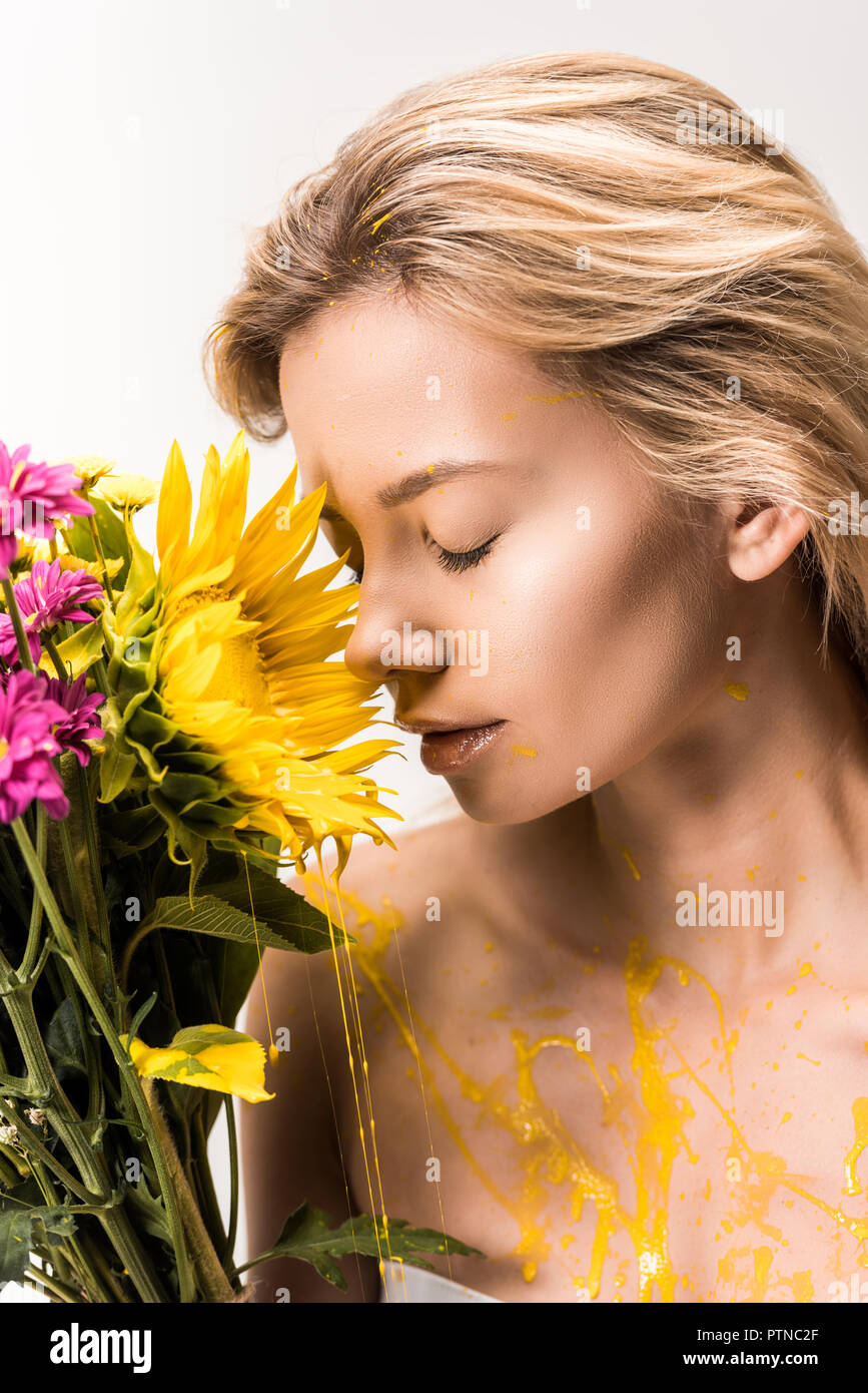 attractive woman with yellow paint on body sniffing bouquet of flowers isolated on white Stock Photo