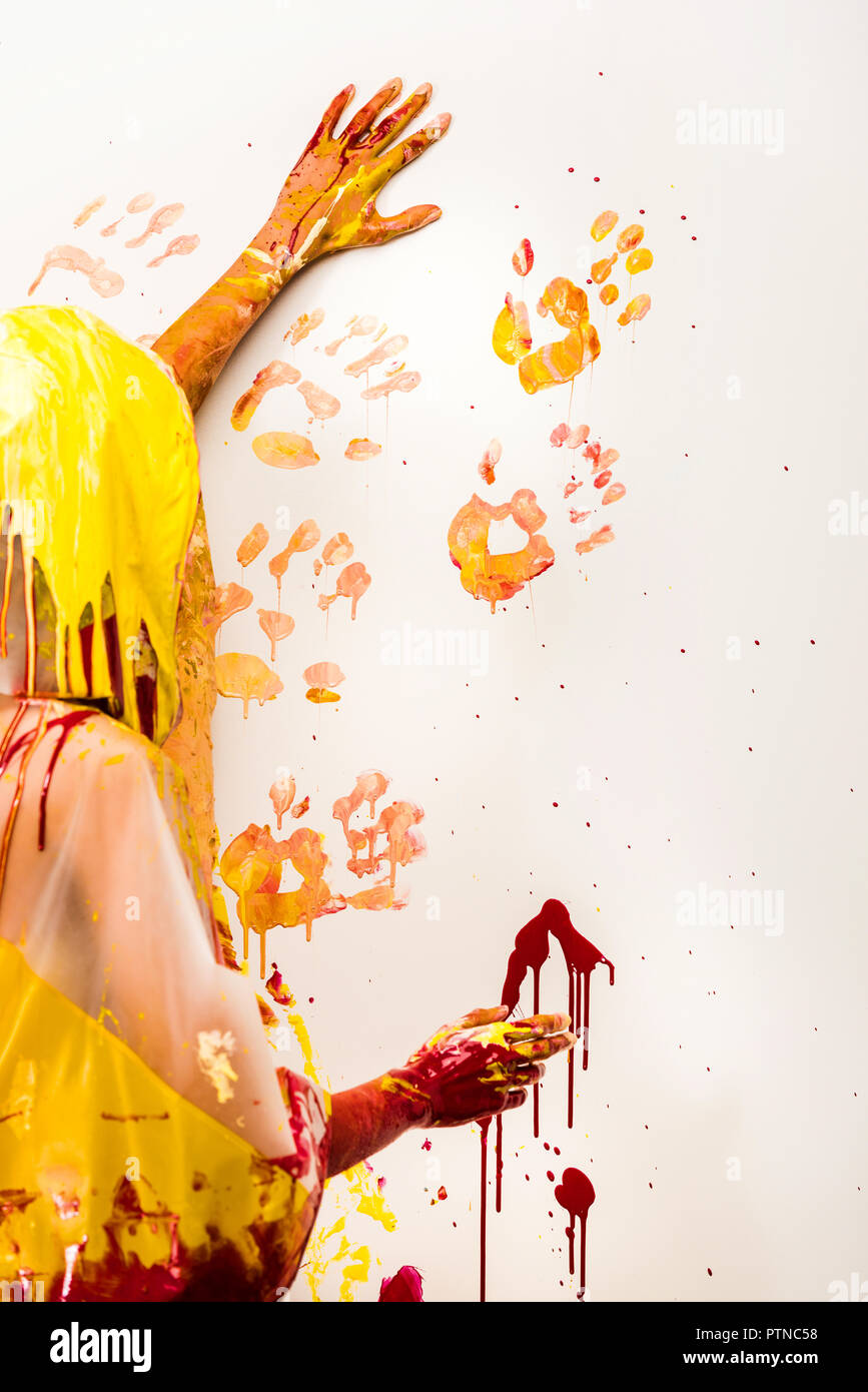 woman in raincoat painting wall with yellow and red hand prints Stock