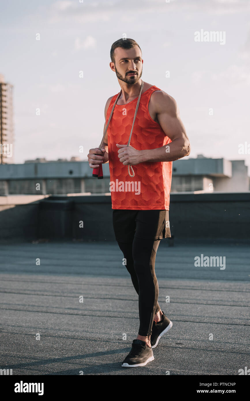 handsome sportive man with jumping rope and red shirt looking away on roof Stock Photo