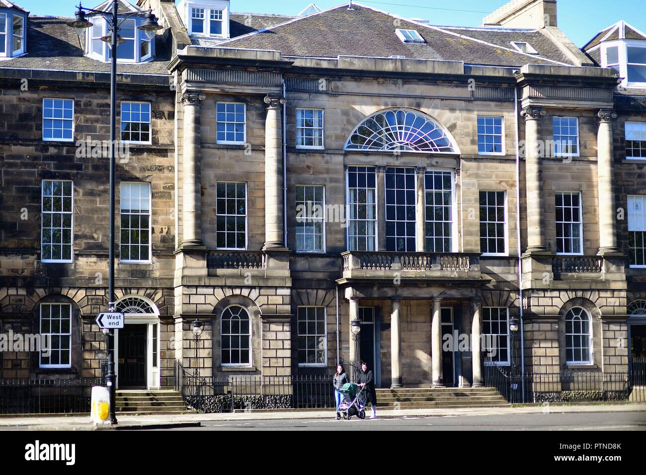 Edinbrugh, Scotland, United Kingdom. Woman crossing the street with a baby carriage within a tidy square in Edinburgh's city center.- Stock Photo