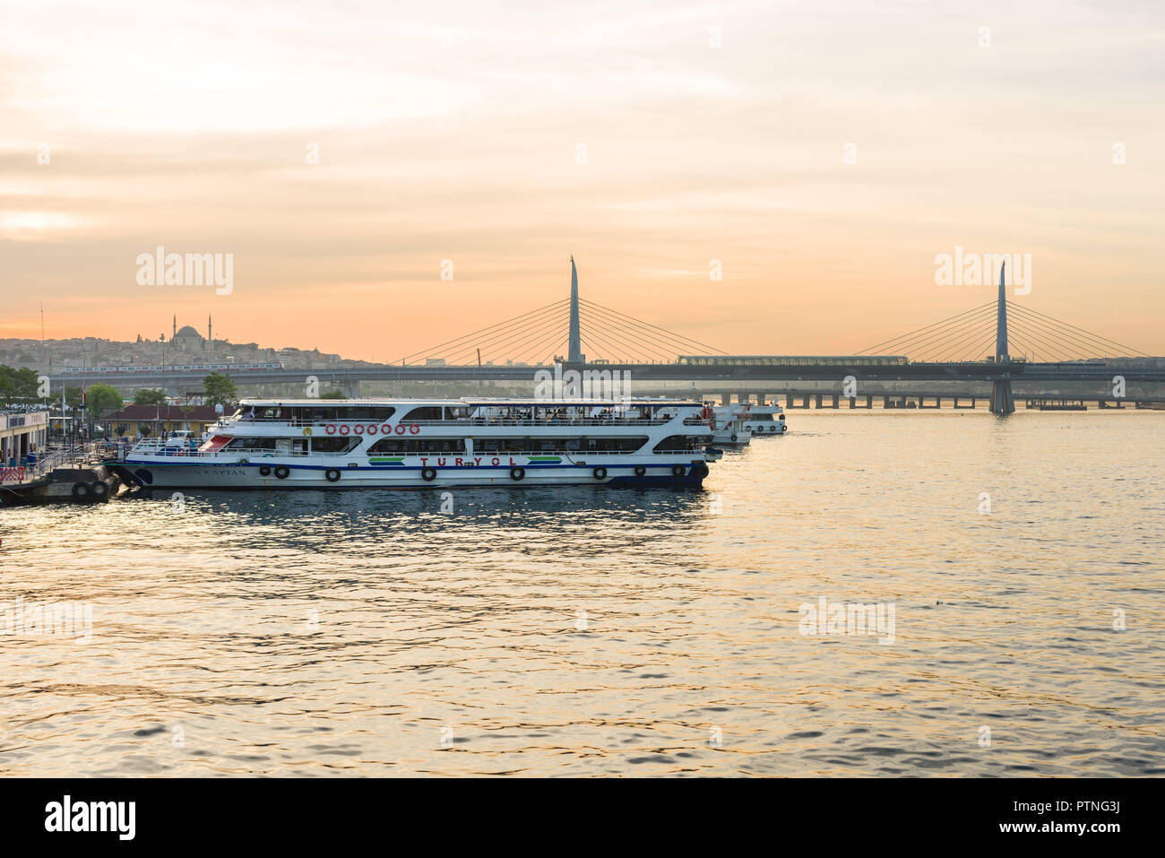 A passenger docked at Eminonu port with Halic bridge in the background at sunset, Istanbul, Turkey Stock Photo