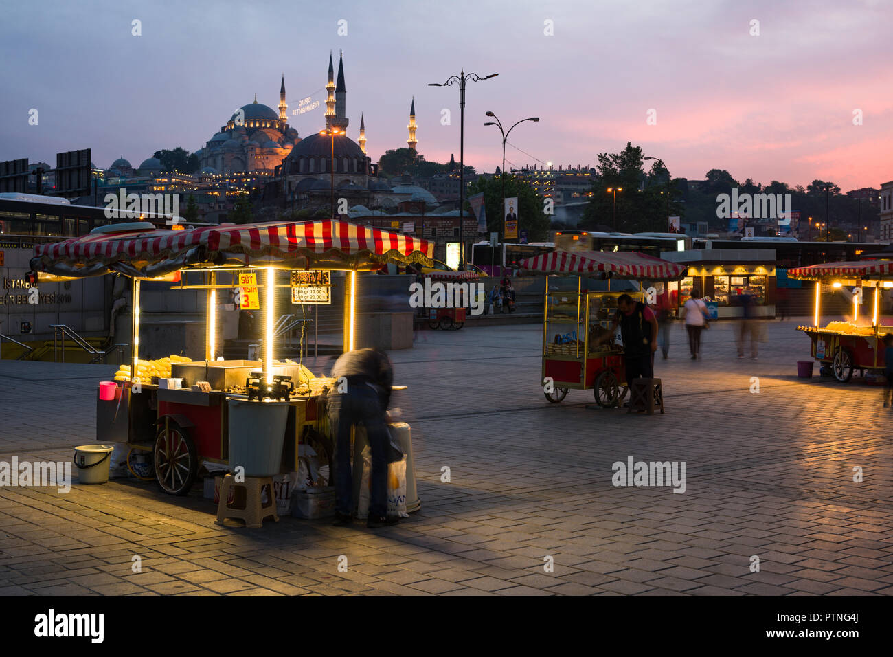 Eminonu bazaar with food stalls and people with Suleymaniye mosque lit up in the background at sunset, Istanbul, Turkey Stock Photo