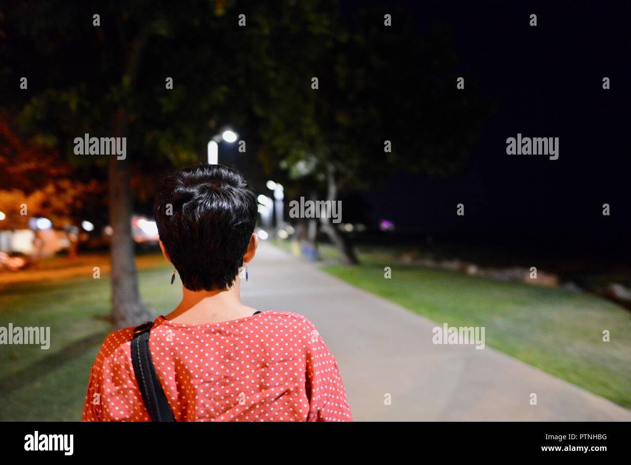 A woman walks alone down a path at night, Townsville, Queensland, Australia Stock Photo