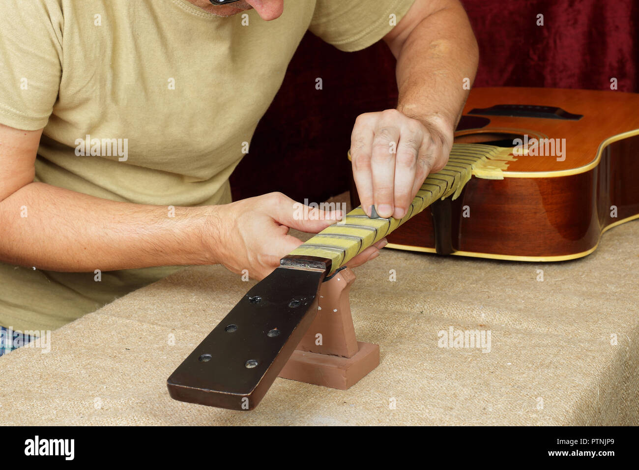 Musical instrument guitar repair and service - Worker polishing guitar neck frets acoustic guitar sandpaper Stock Photo