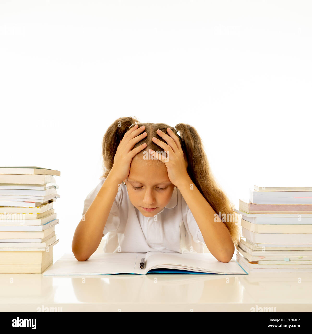 Sad and tired cute schoolgirl with blond hair sitting in stress doing homework overwhelm with too much study and textbooks in children education acade Stock Photo