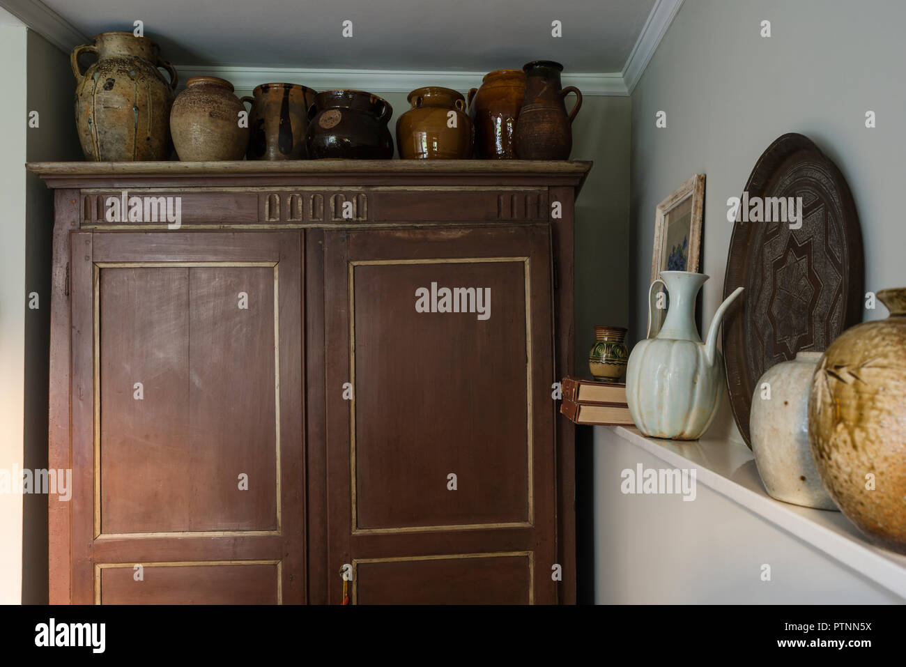 French salt-glazed cruches jugs are arranged along the top of the rustic French painted armoire Stock Photo