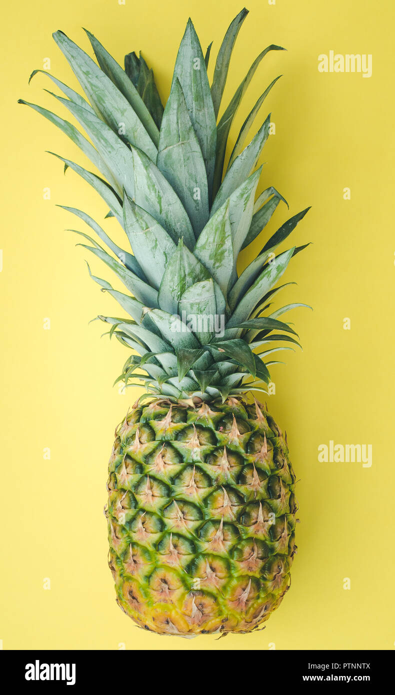 A whole, fresh pineapple with textured and patterned skin on a yellow background Stock Photo