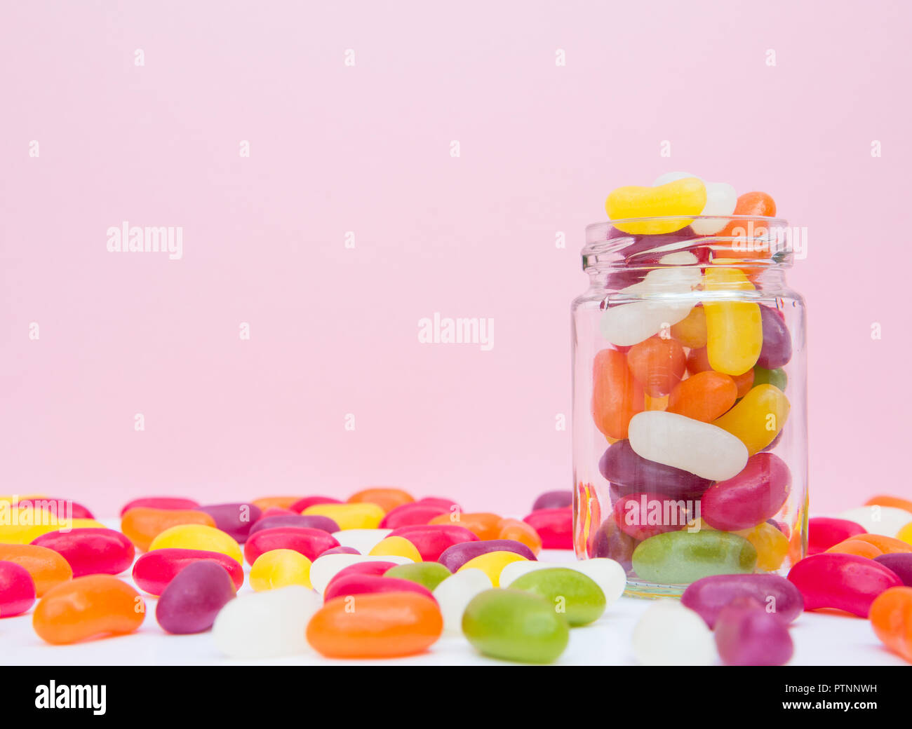 A glass jar full of chewy jelly bean candy in a sweet shop with a pink background and copy space Stock Photo
