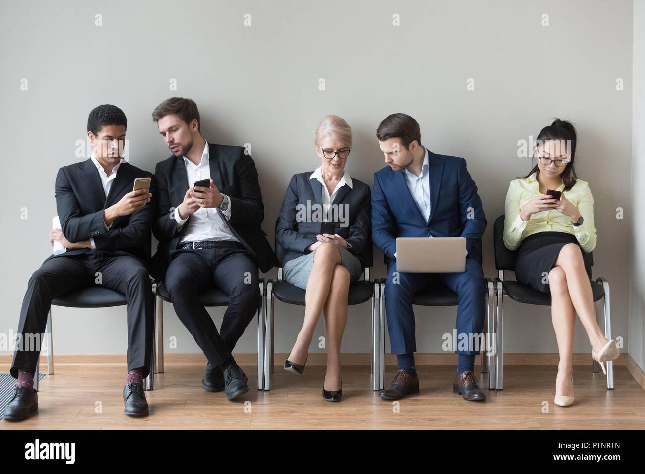 Diverse work candidates sit in queue using gadgets before interv Stock Photo