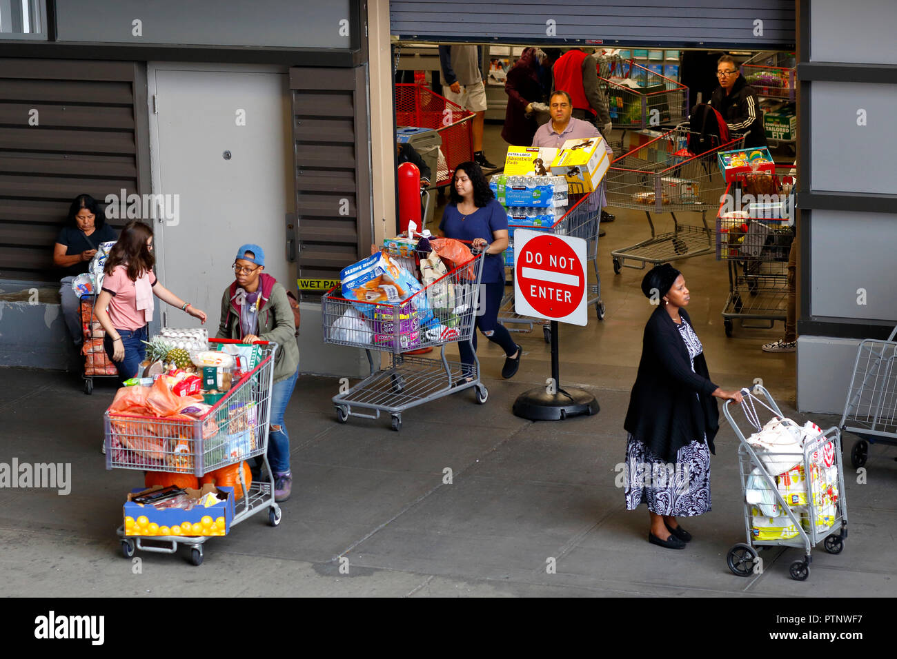 Shoppers exiting a Costco warehouse club supermarket with carts full of bulk, and supersized groceries, in the East Harlem neighborhood of Manhattan Stock Photo