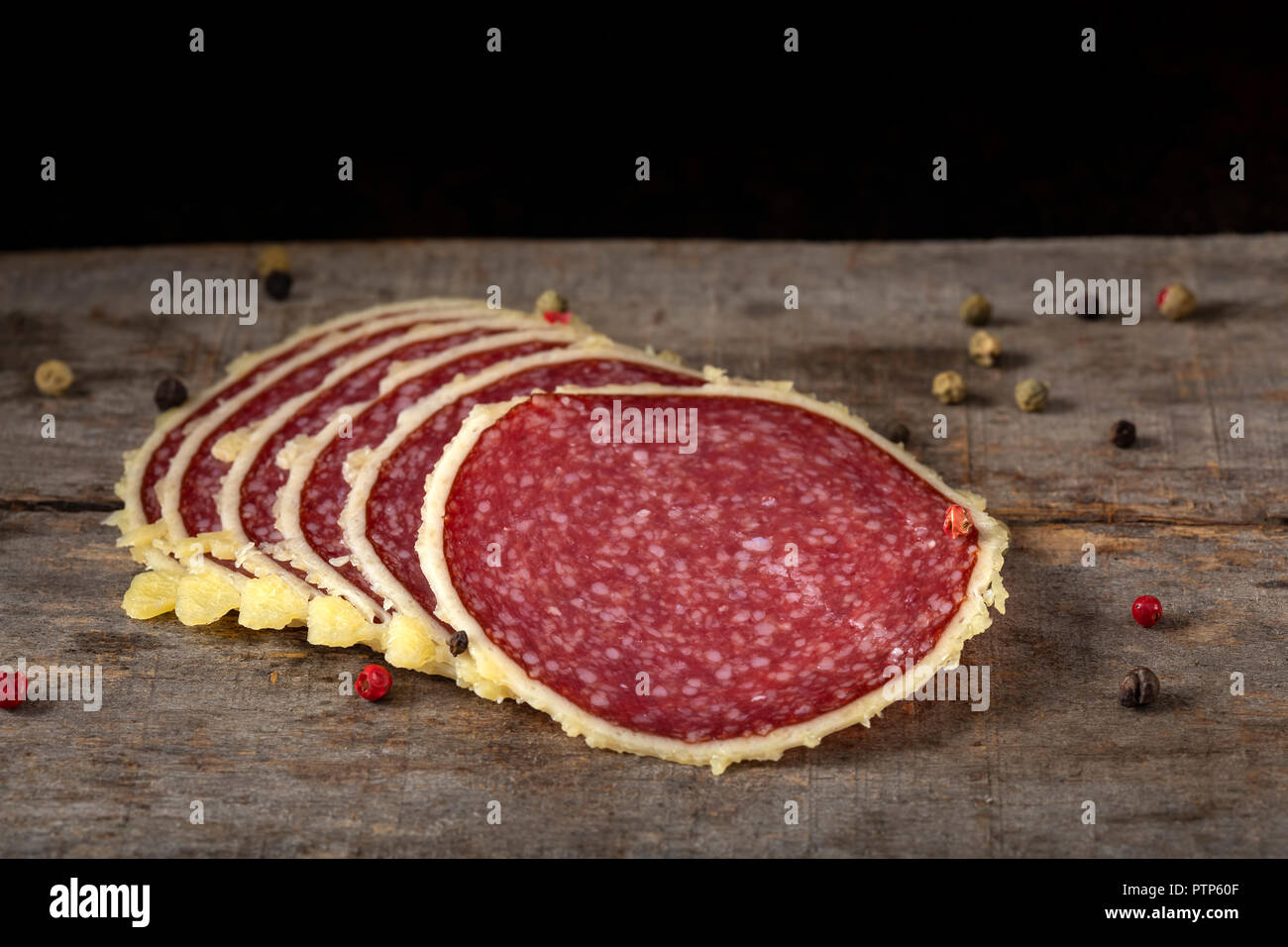 Slices of salami surrounded by parmesan cheese with peppercorns on wooden rustic bakground Stock Photo