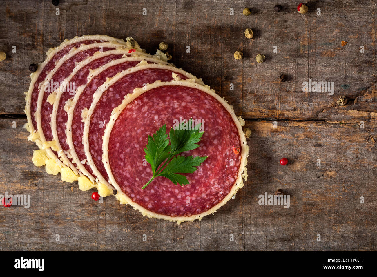 Slices of salami surrounded by parmesan cheese with peppercorns on wooden rustic bakground - top view Stock Photo