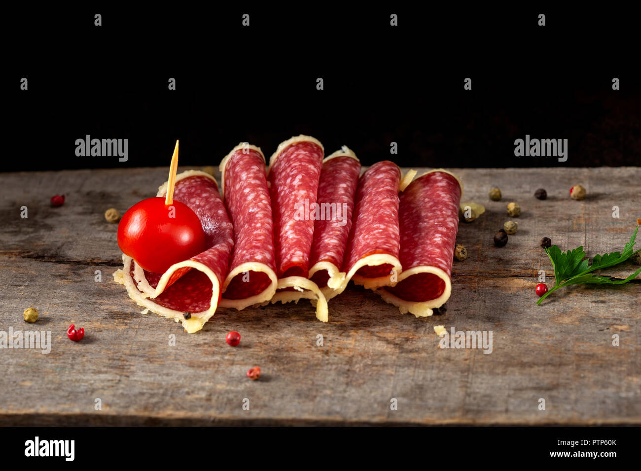 Slices of salami surrounded by parmesan cheese with peppercorns and cherry tomato on wooden rustic bakground Stock Photo