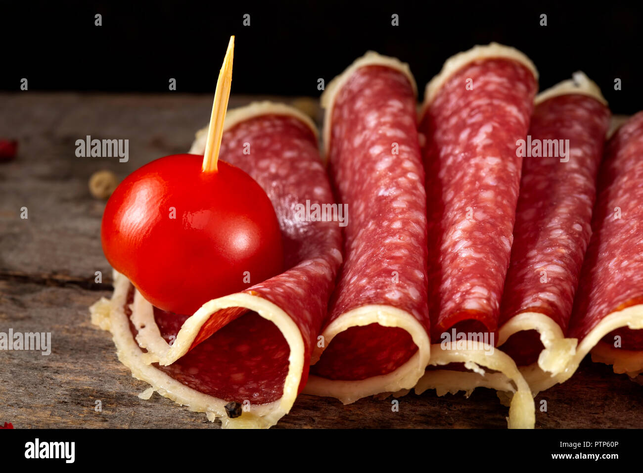 Slices of salami surrounded by parmesan cheese with peppercorns and cherry tomato - close up view Stock Photo