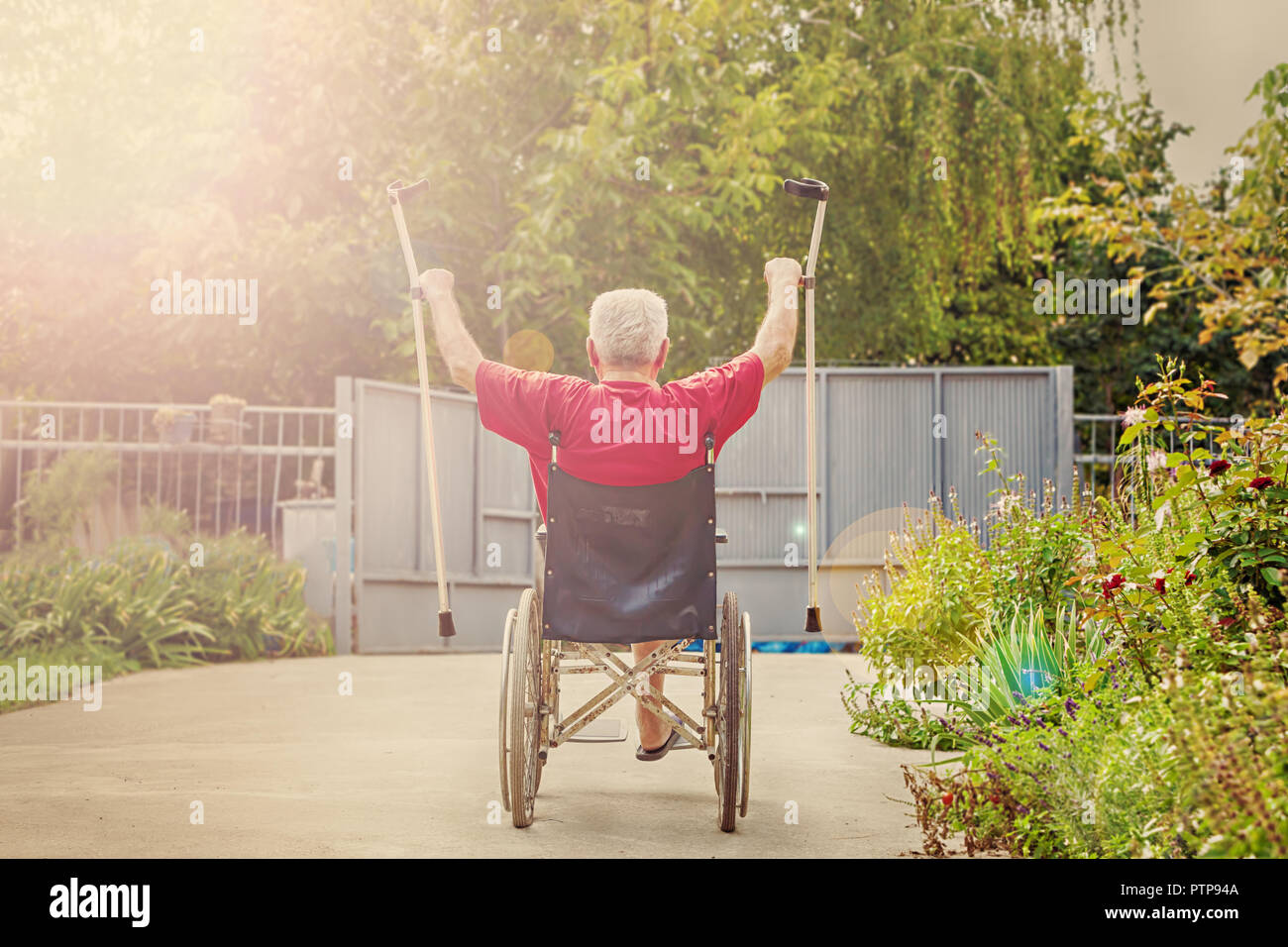 Back View of an older, handicapped man, arms and crutches raised in happiness, sunflare Stock Photo
