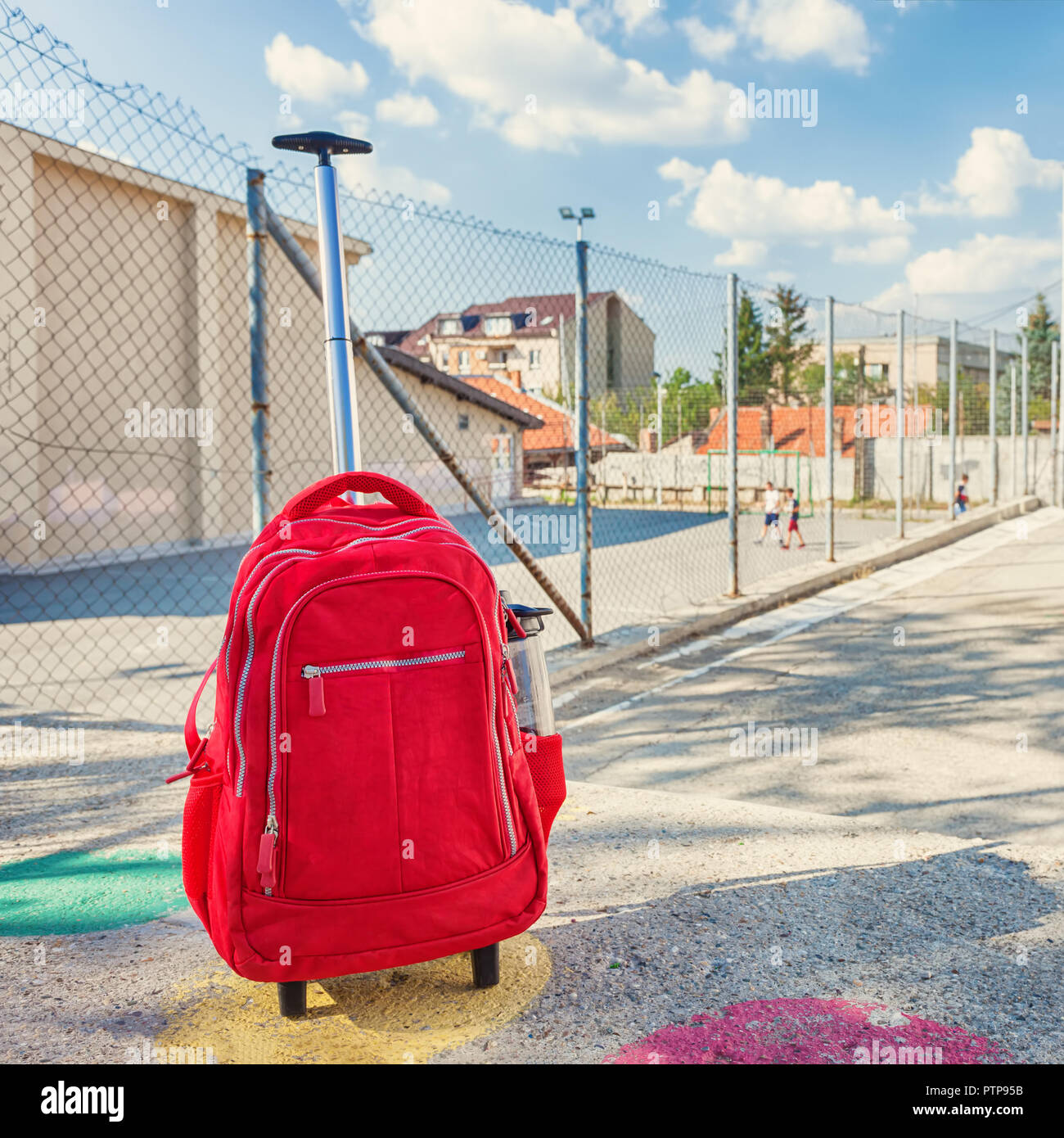 Modern red weightless school bag with handle and wheels on the schoolyard Stock Photo
