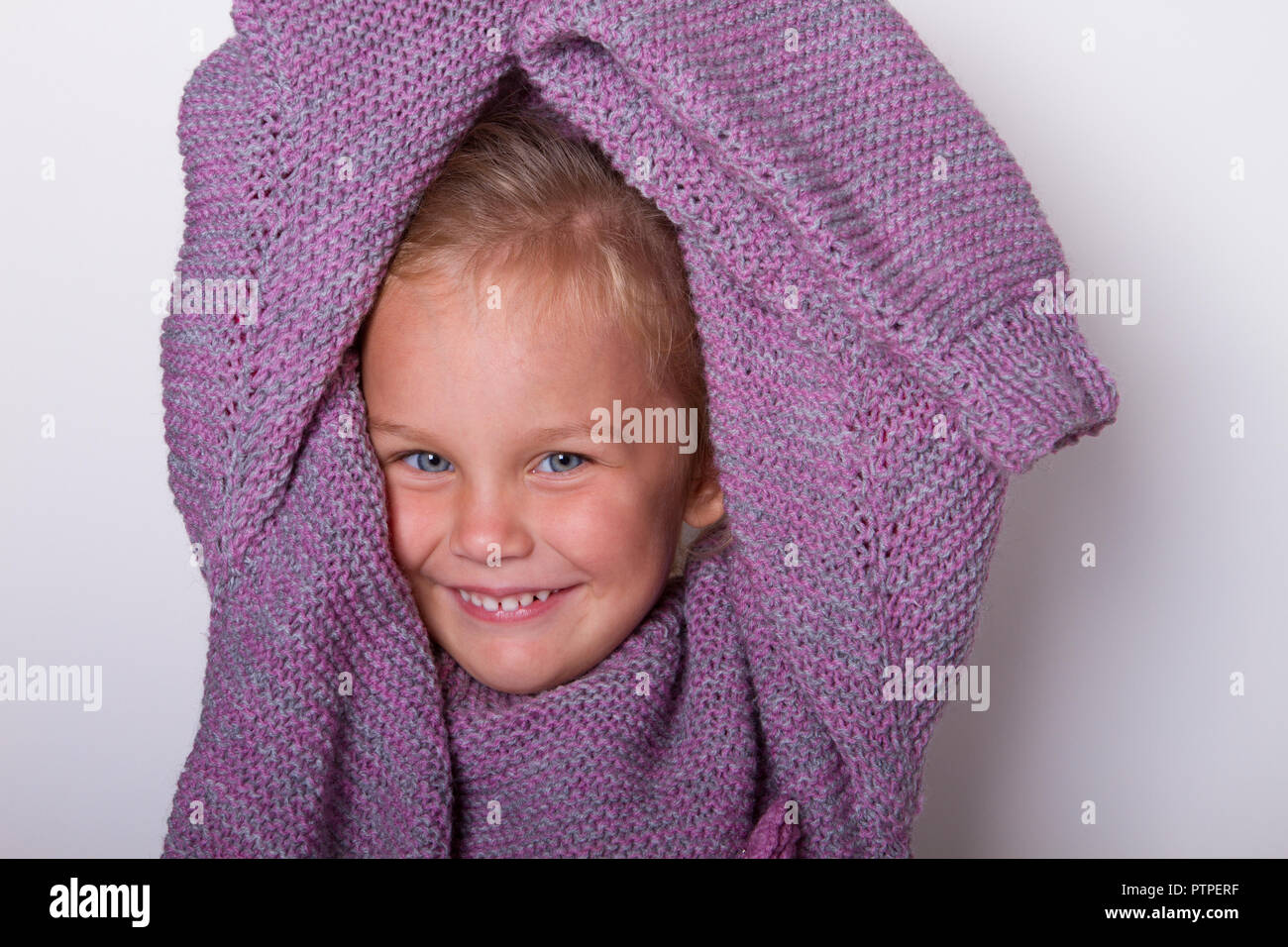 happy beautiful little girl wore a knitted lilac mom's sweater and fooled around in it. concept of childhood, small size, to grow. Stock Photo