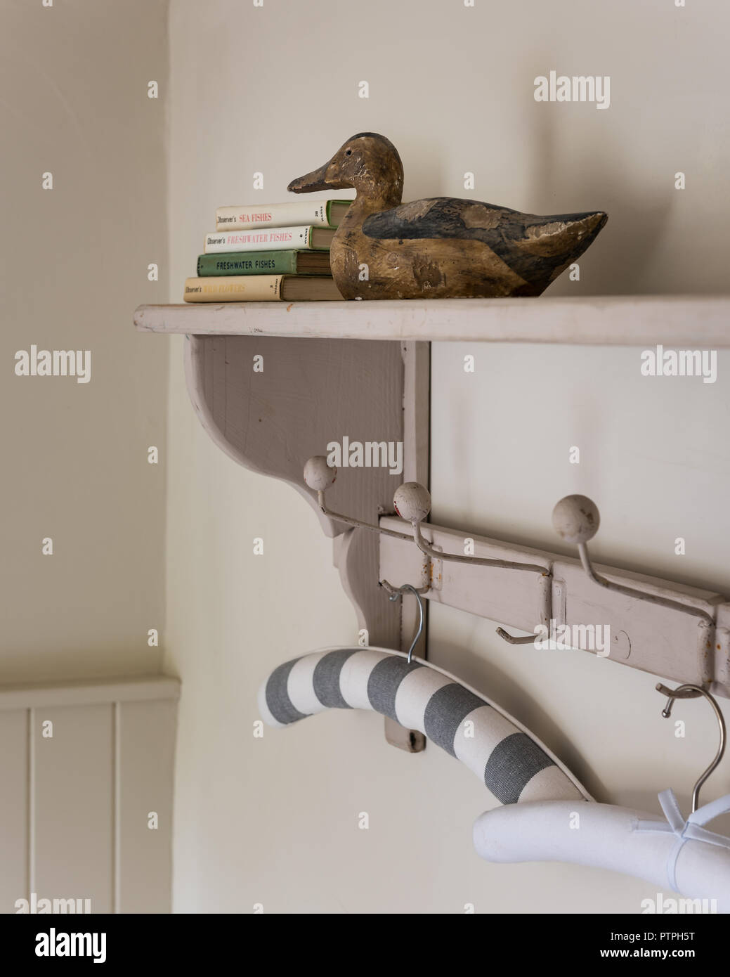 Decoy duck and clothes hanger with hardback books on shelf in 18th century Norfolk cottage Stock Photo