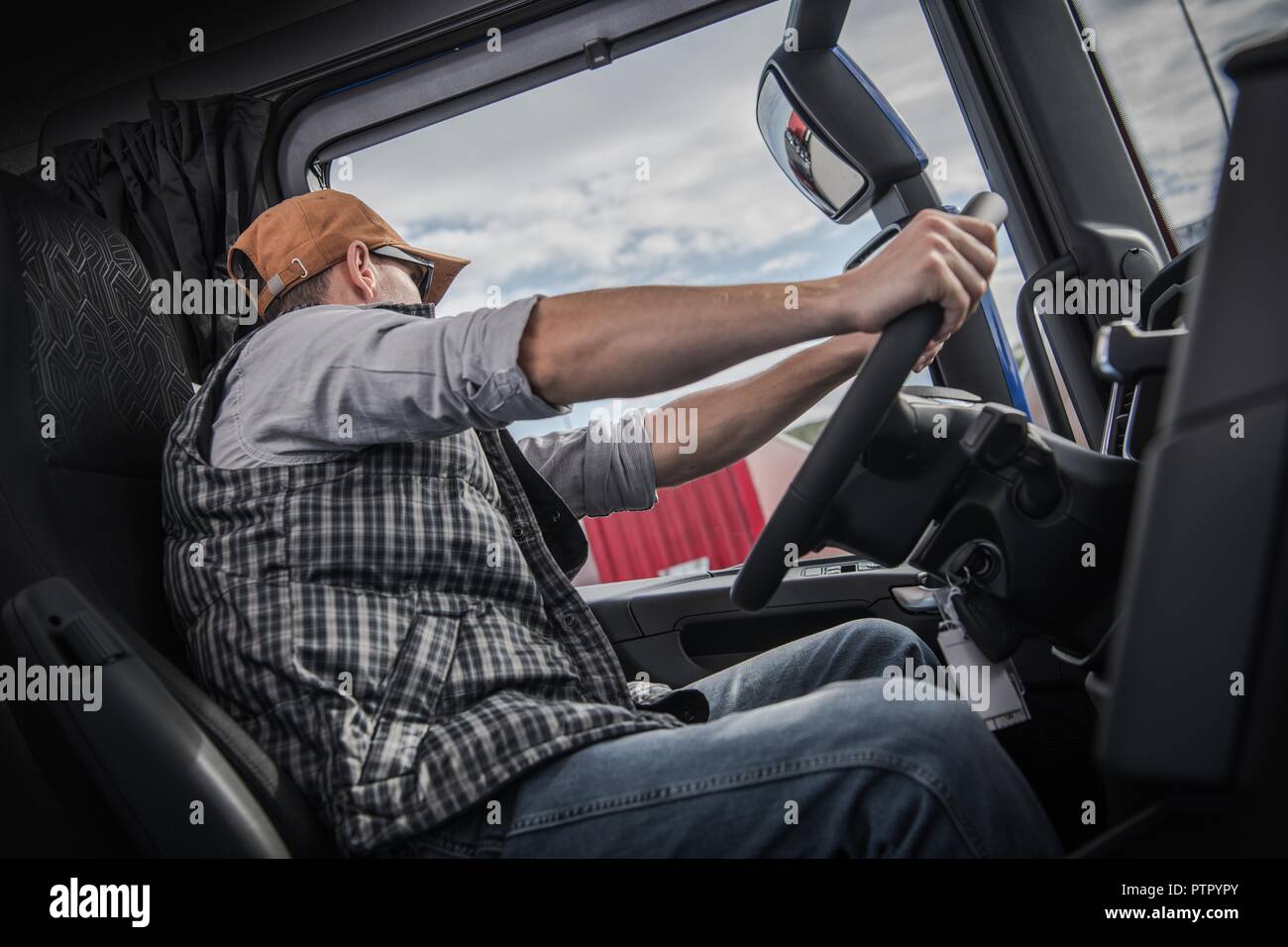 Caucasian Trucker in His 30s Behind Modern Semi Truck Wheel. Transportation Industry. Stock Photo