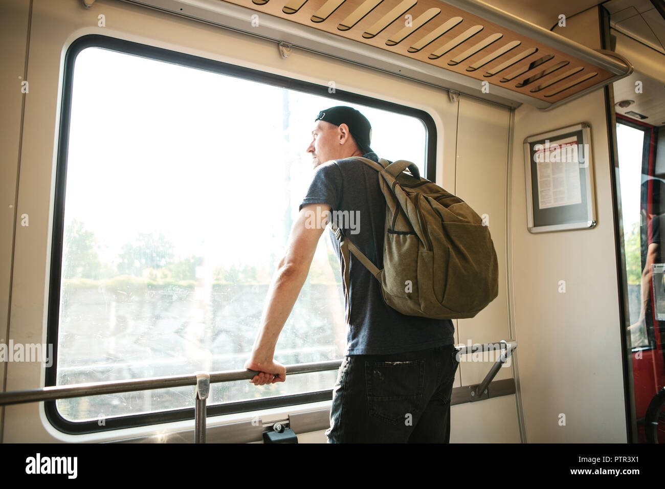 A young guy with a backpack inside the train looks out the window while
