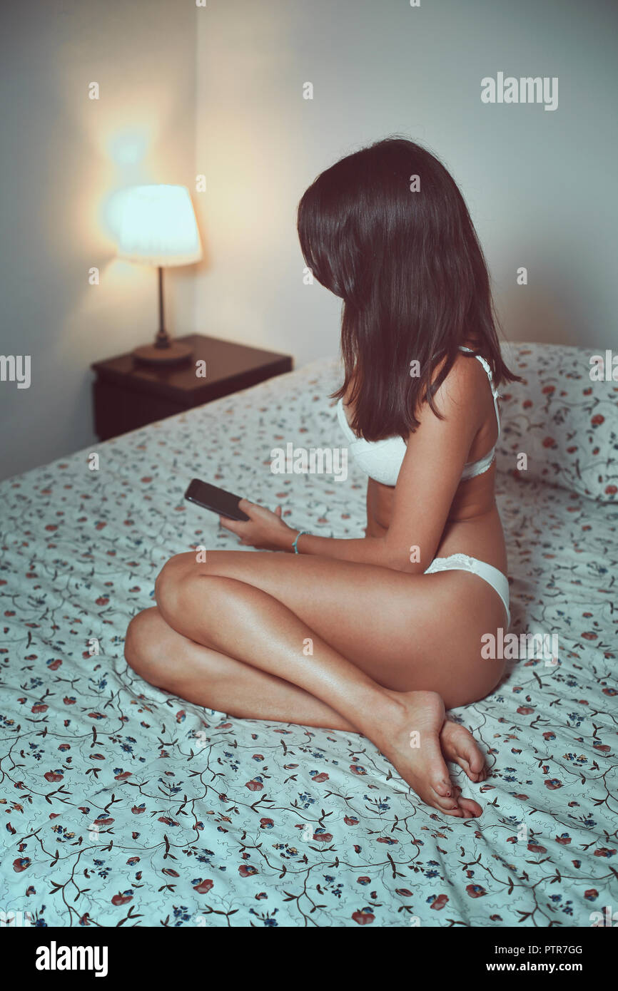 Sensual girl on a bed with smartphone