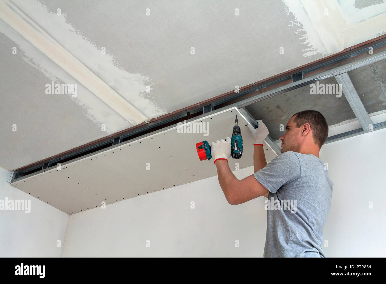 Young Man In Usual Clothing And Work Gloves Fixing Drywall
