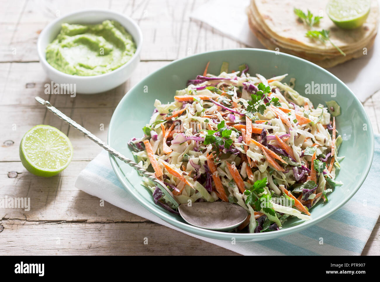Coleslaw made from cabbage, carrots and various herbs, served with tortillas and guacamala on a wooden background. Selective focus. Stock Photo