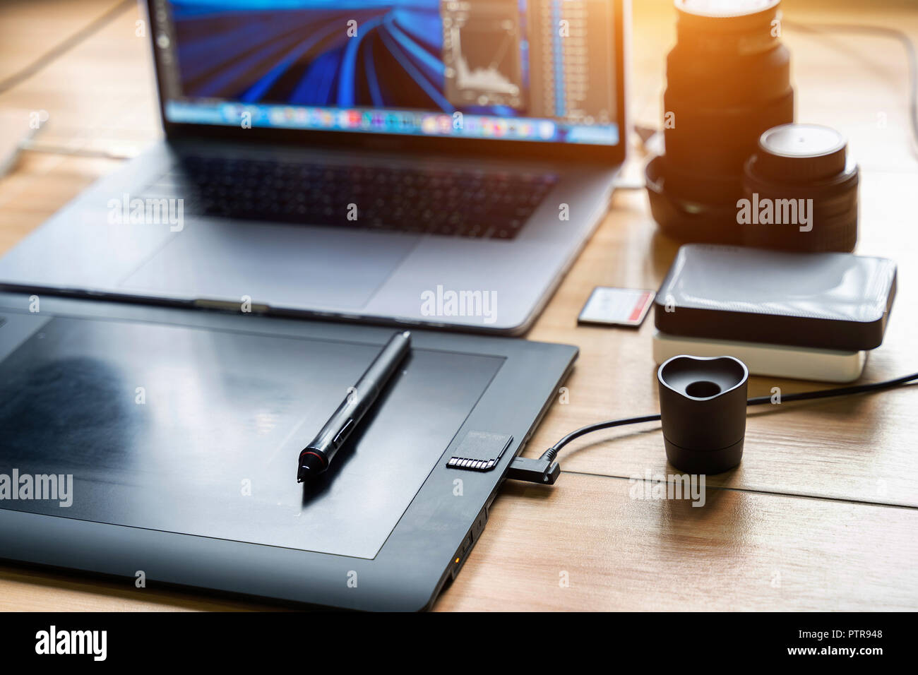 Drawing tablet and laptop computer, harddisk, memory card, camera lens on table. Photographer concept. Stock Photo