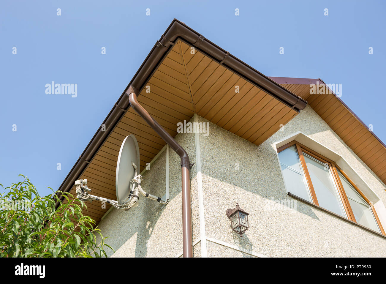 Bottom view detail of new modern house top with decorative lamp and satellite dish on stucco walls plastic attic window gutter pipe system on blue s