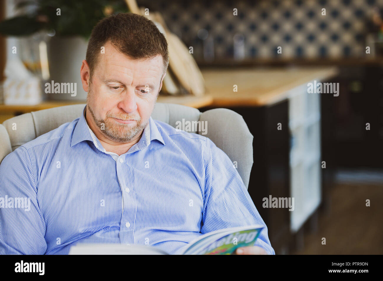Man in business attire reading a magazine in a co-working space that functions as his office Stock Photo