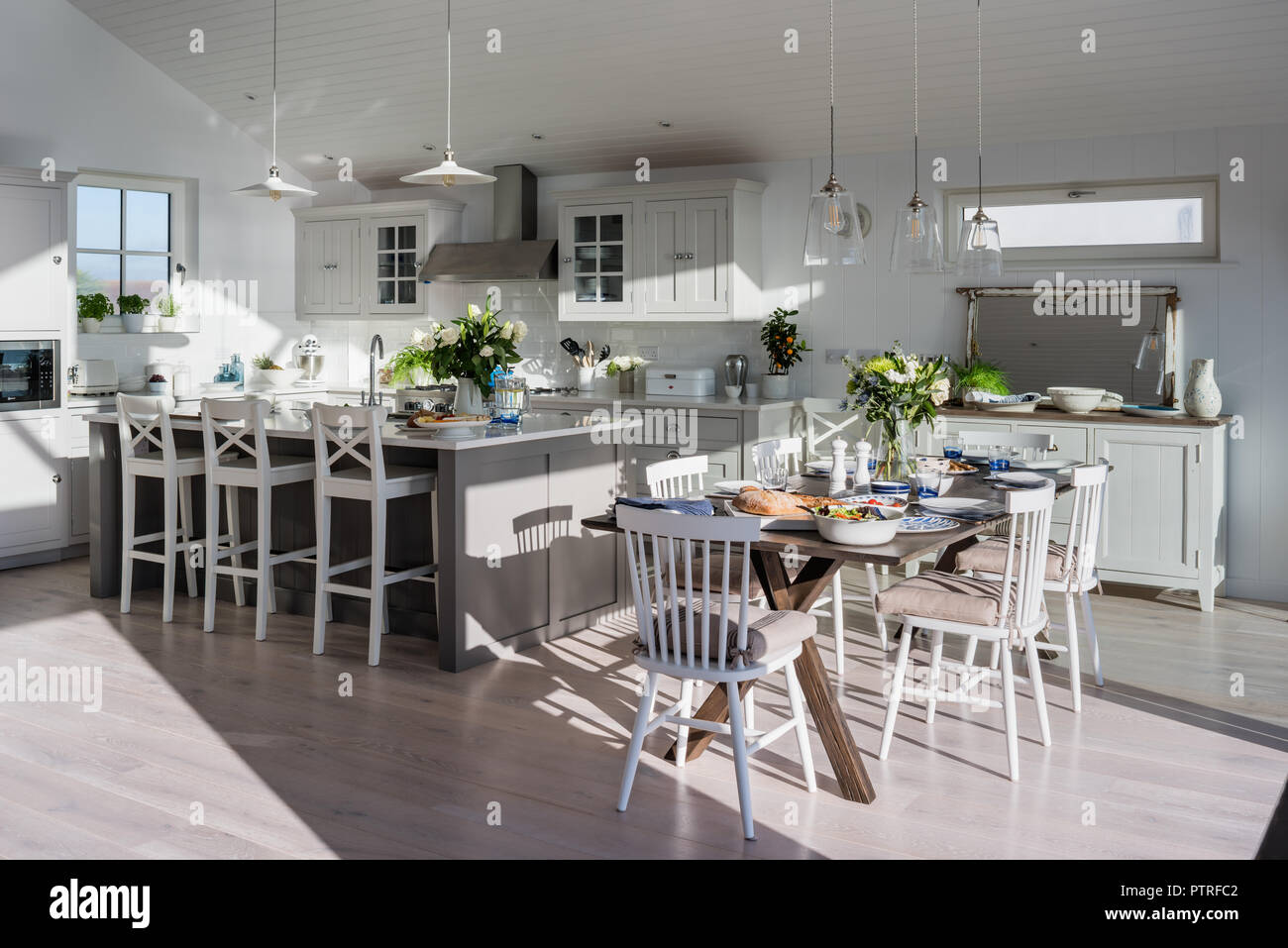 Open plan kitchen and dining room with sea views Bar stools at island unit with dining table and chairs in sunlit coastal home Stock Photo