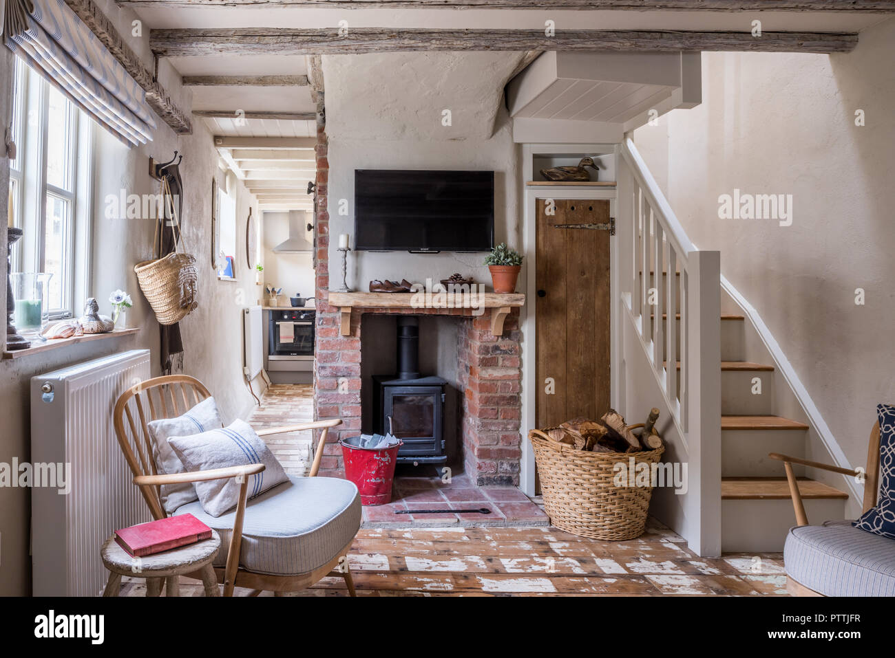 Stripped Ercol-style armchair and wall mounted TV above exposed brick fireplace with woodburner Stock Photo