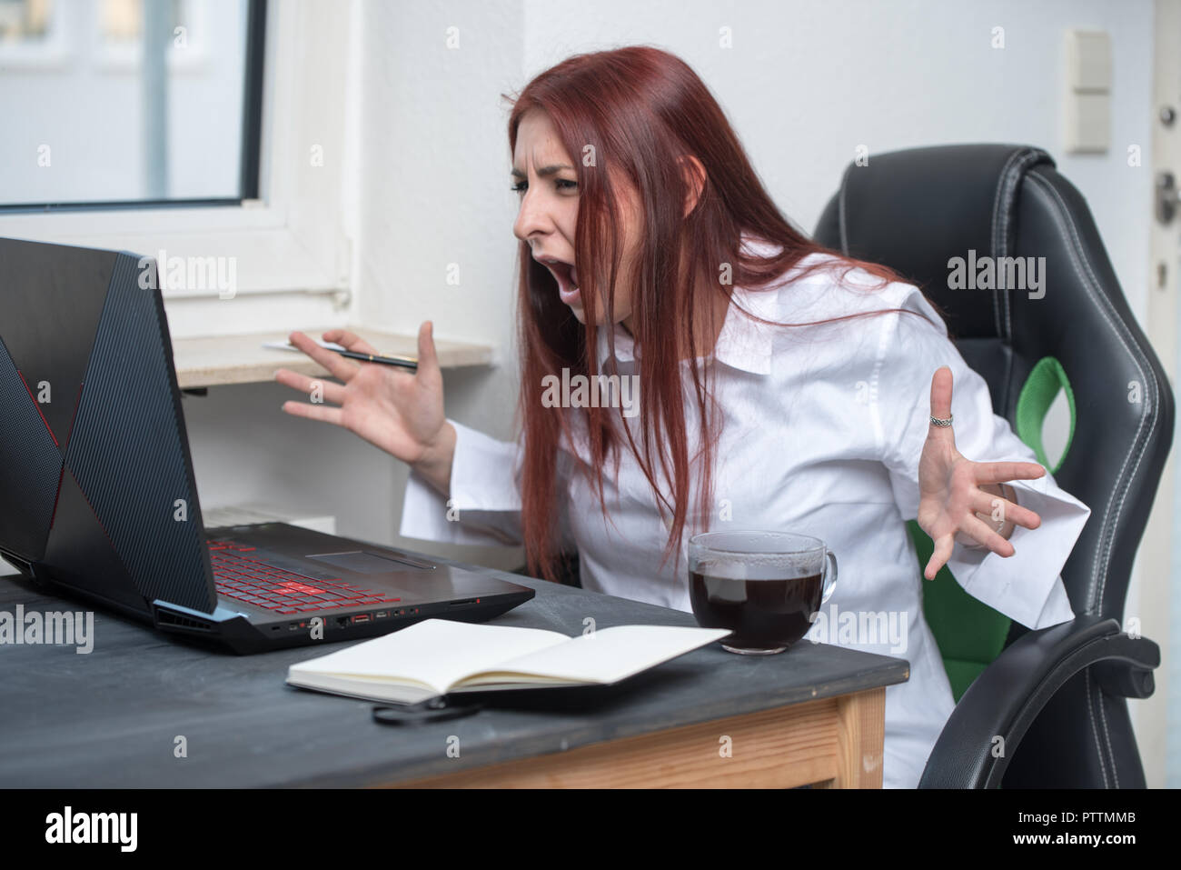 stressed, angry young woman sitting at a desk and screaming at the computer Stock Photo