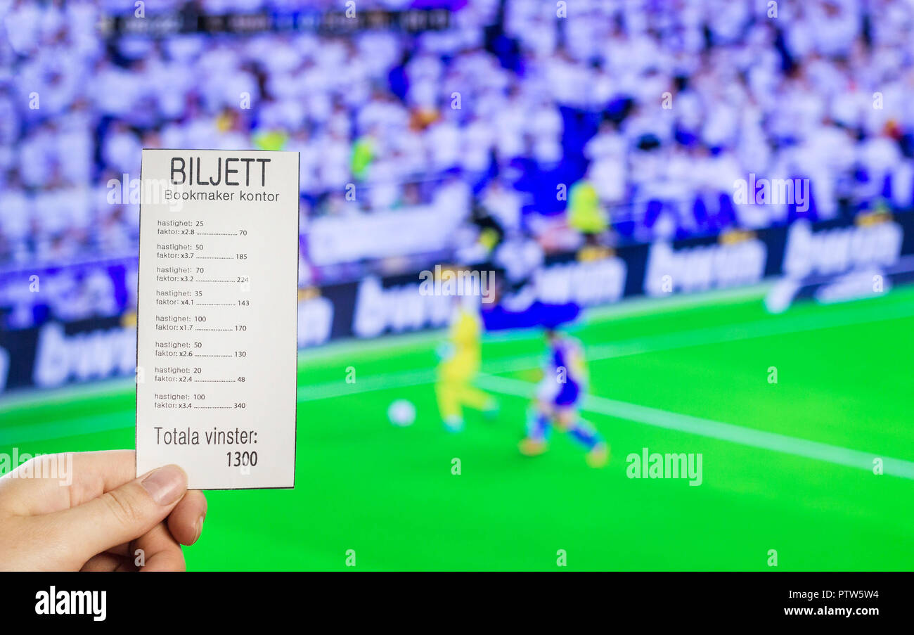 A woman's hand holds a bookmaker's ticket against the backdrop of a game of football, sports betting, the bookmaker's office. Biljett Bookmaker kontor-Ticket bookmakers office, hastighet-bet, faktor-ratio, totala vinster -total win Stock Photo