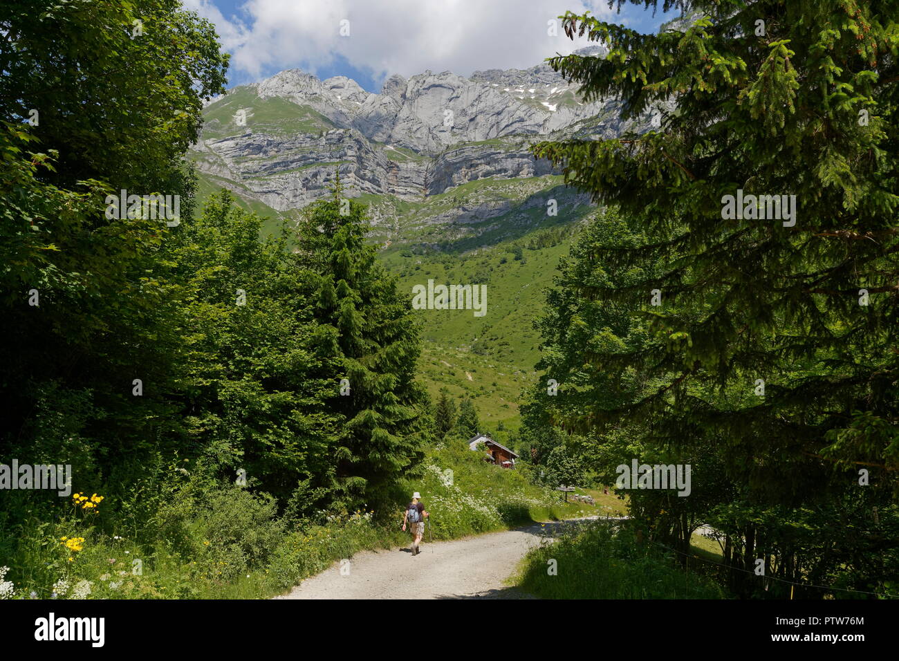 Female hiker walking towards a distant restaurant on the off road tracks in the valleys of the french alps nr Montmin France Stock Photo