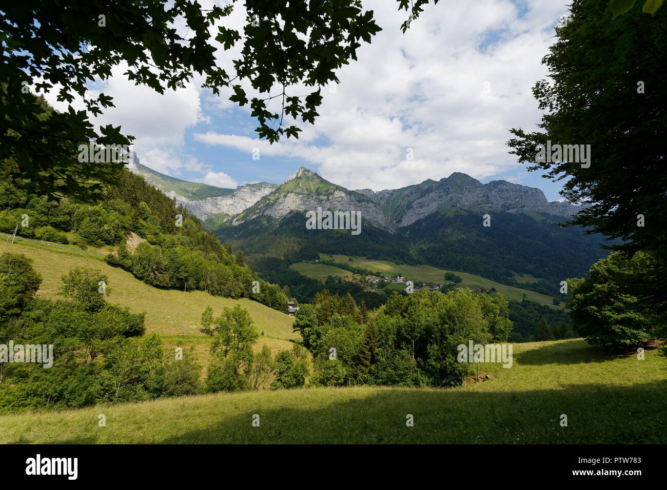 View of  Montmin nestled in the valley through tree foliage below Col de la Forclaz France Stock Photo