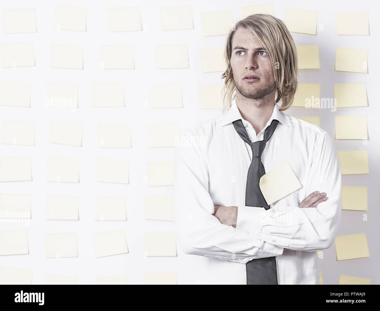 Junger Mann steht in Hemd und Krawatte vor Postit-Wand, verschraenkte Arme (model-released) Stock Photo