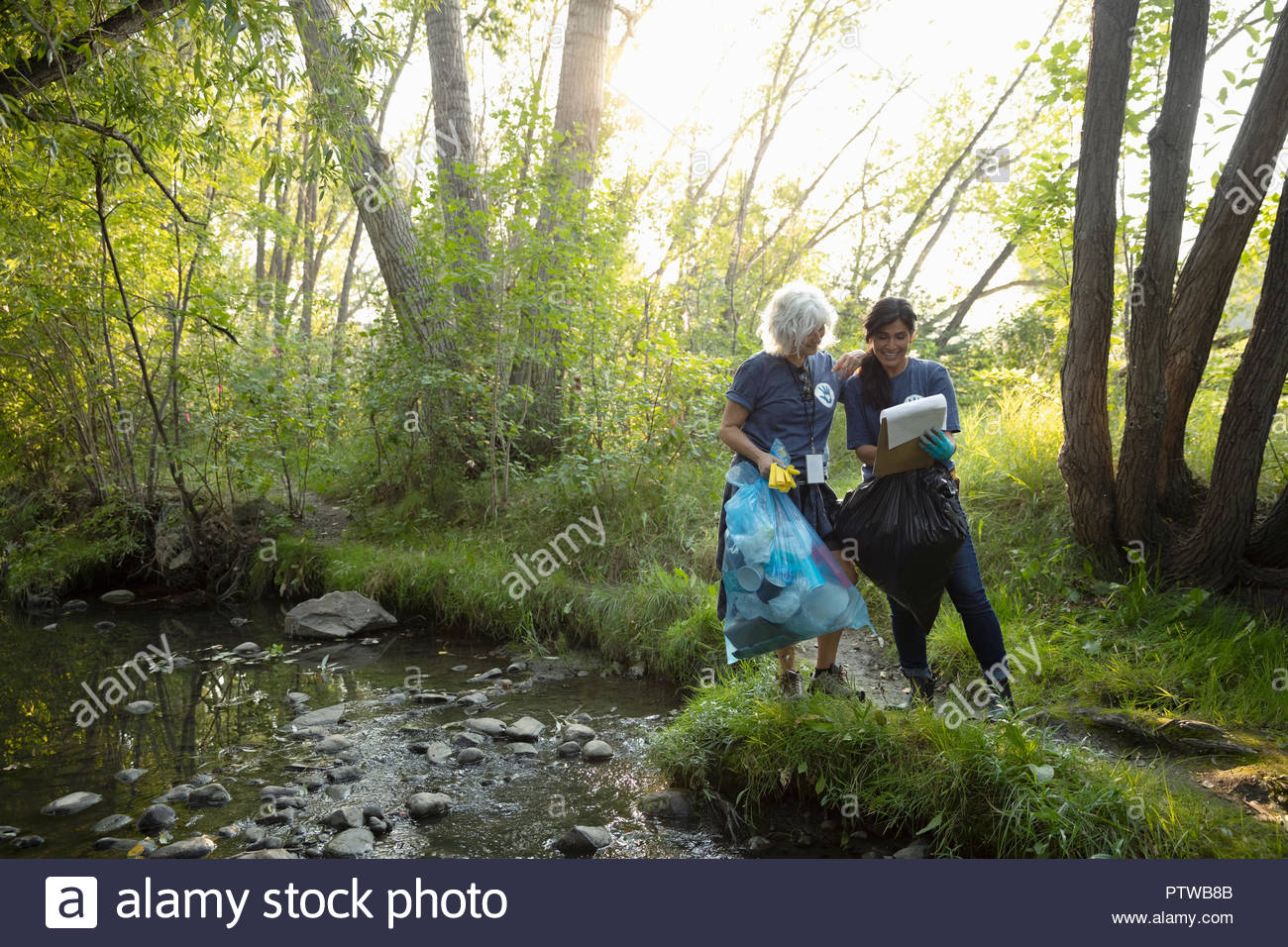 Women with clipboard and garbage bag volunteering, cleaning up garbage in stream Stock Photo