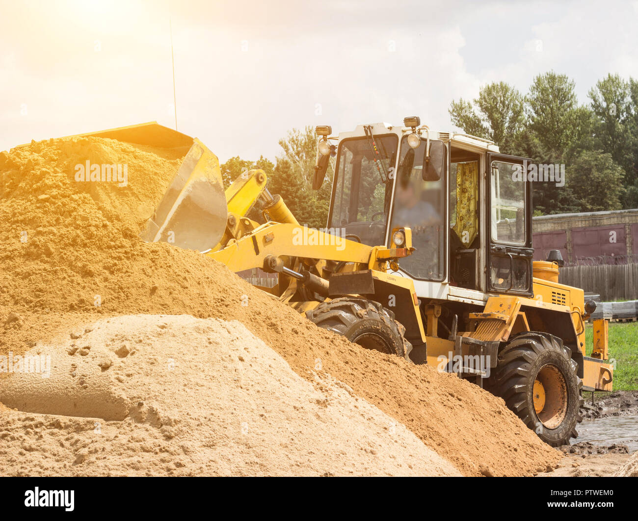 Yellow tractor loader is picking up a bucket of earth, mechanical, ladle with earth and sun Stock Photo