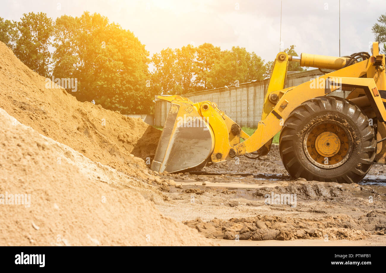 Yellow tractor loader is picking up a bucket of earth, mechanical, ladle with earth and sun Stock Photo