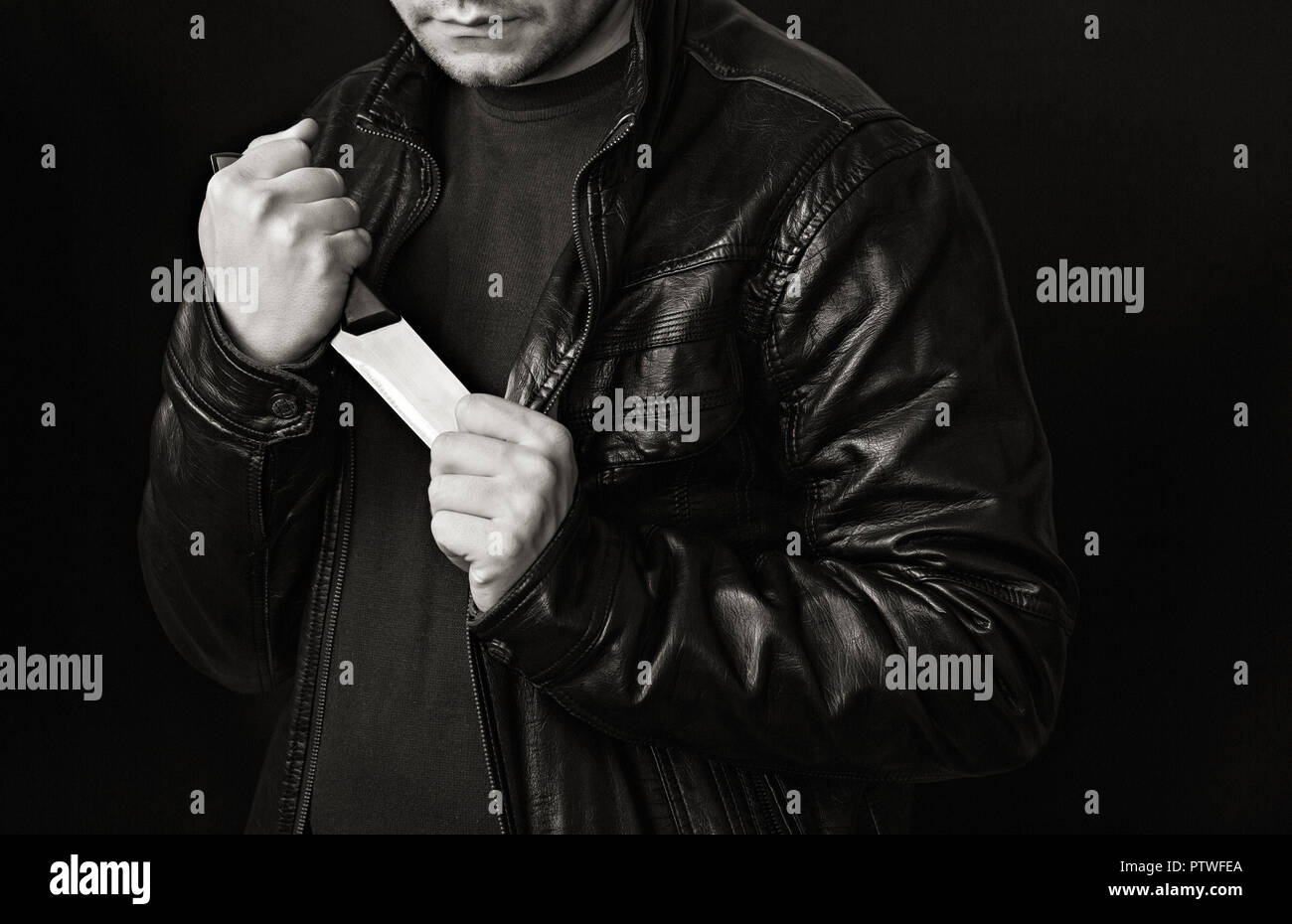 A man takes a knife out of a jacket, a black background, black and white Stock Photo