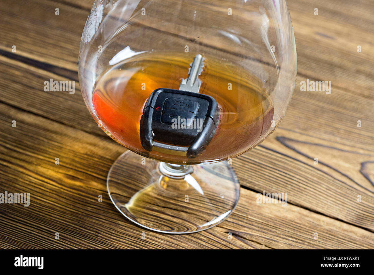 Car key in a glass with alcohol, wooden background, close-up Stock Photo