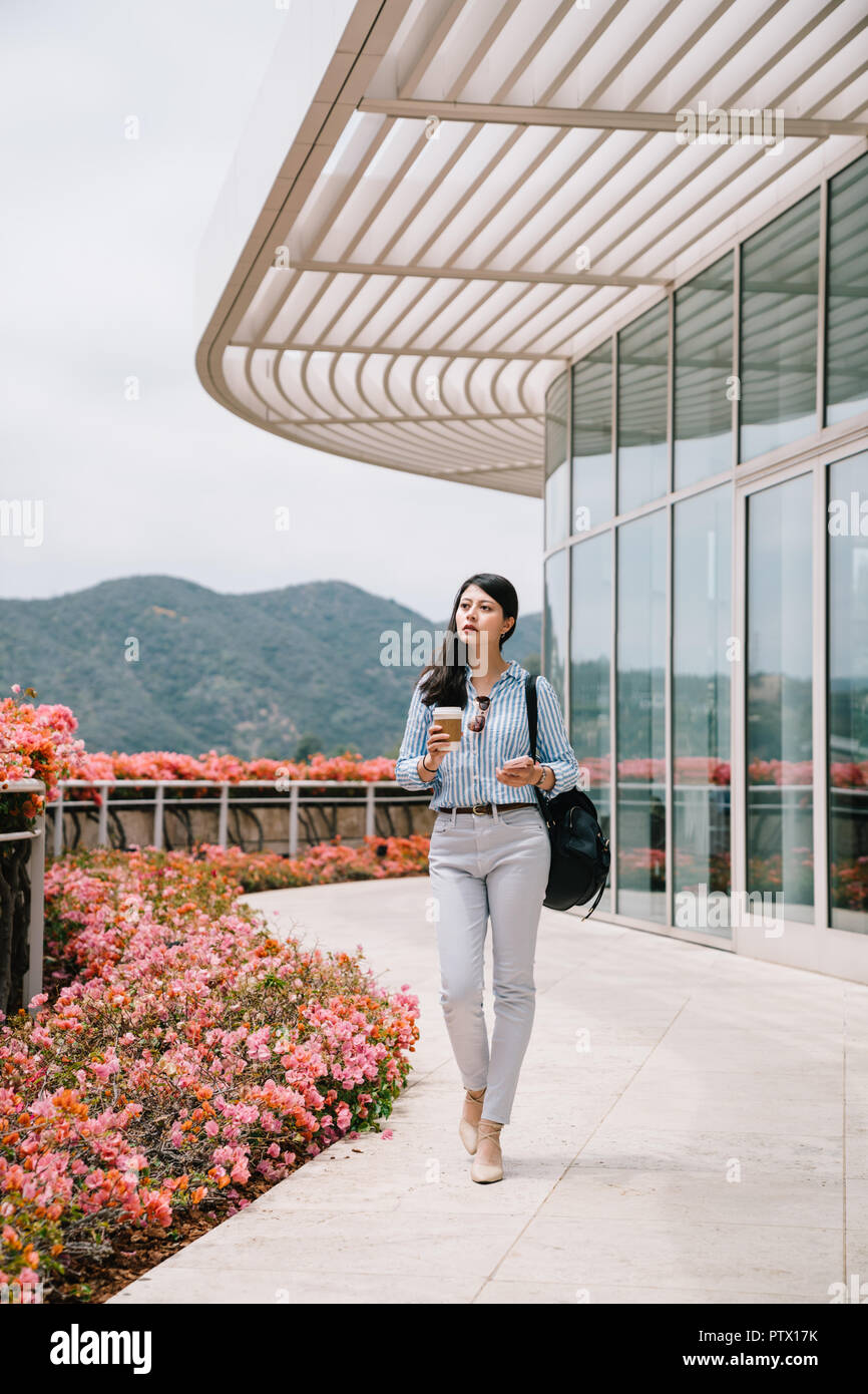 an elegant office lady holding coffee walking pass through the garden and going to work Stock Photo