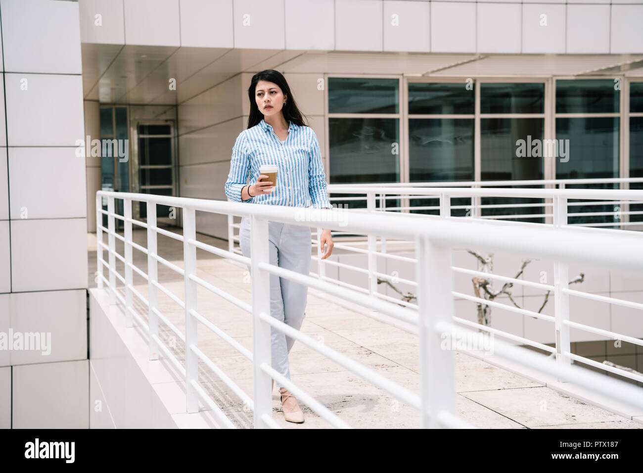 a full length photo of an elegant lady walking through the bridge to another building Stock Photo