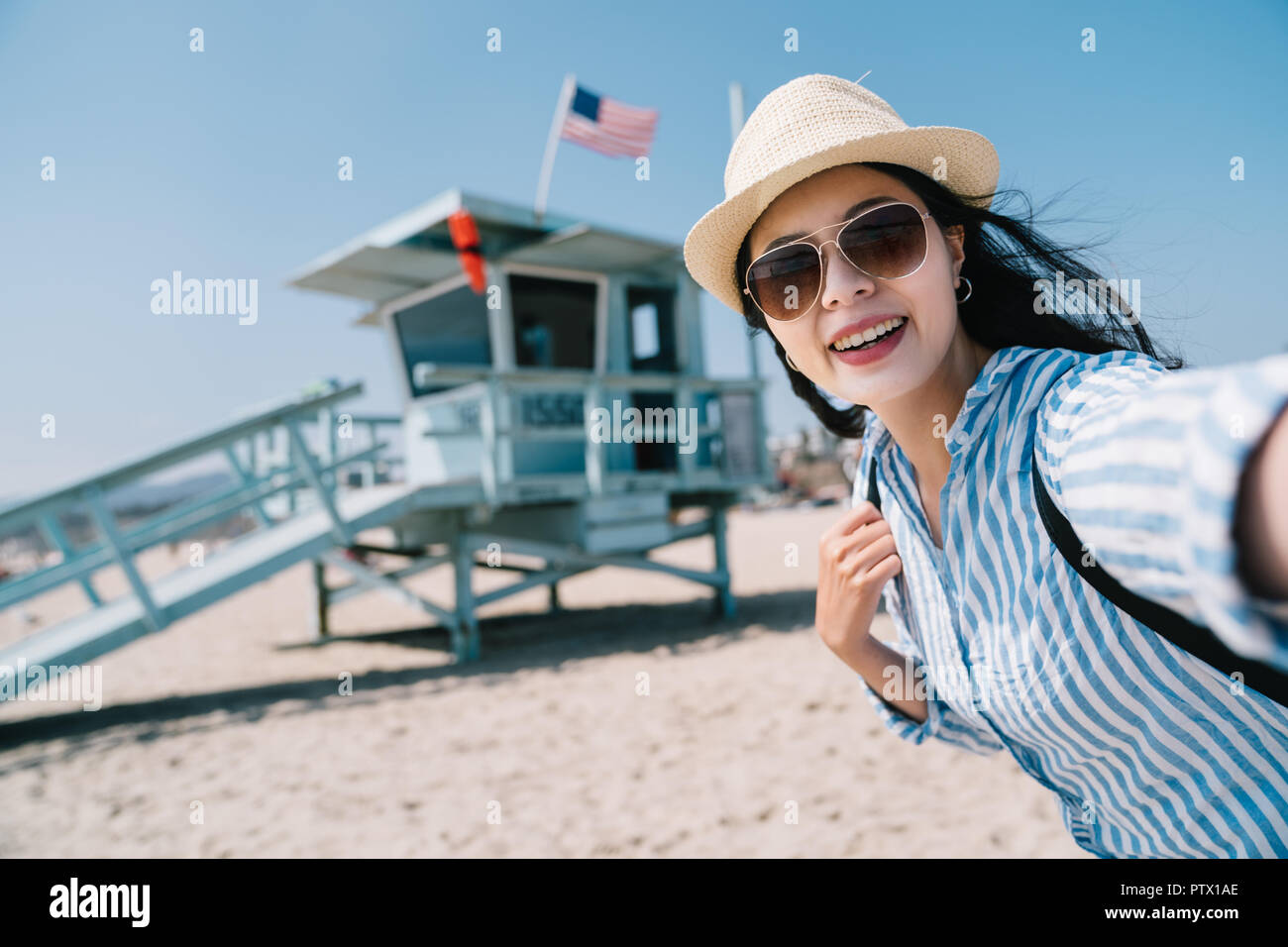a female traveler taking selfie with the lifeguard station with a big smile Stock Photo