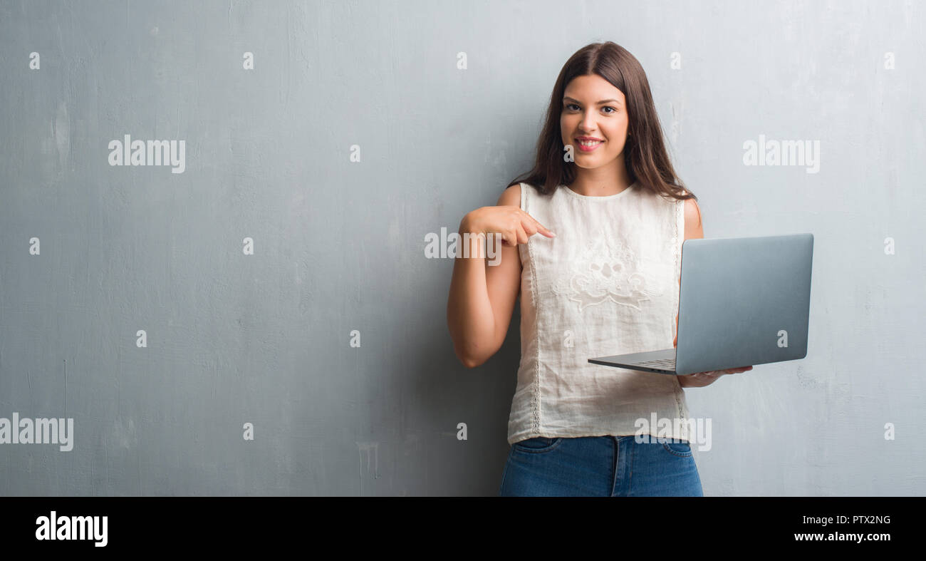 Young brunette woman over grunge grey wall using computer laptop with ...
