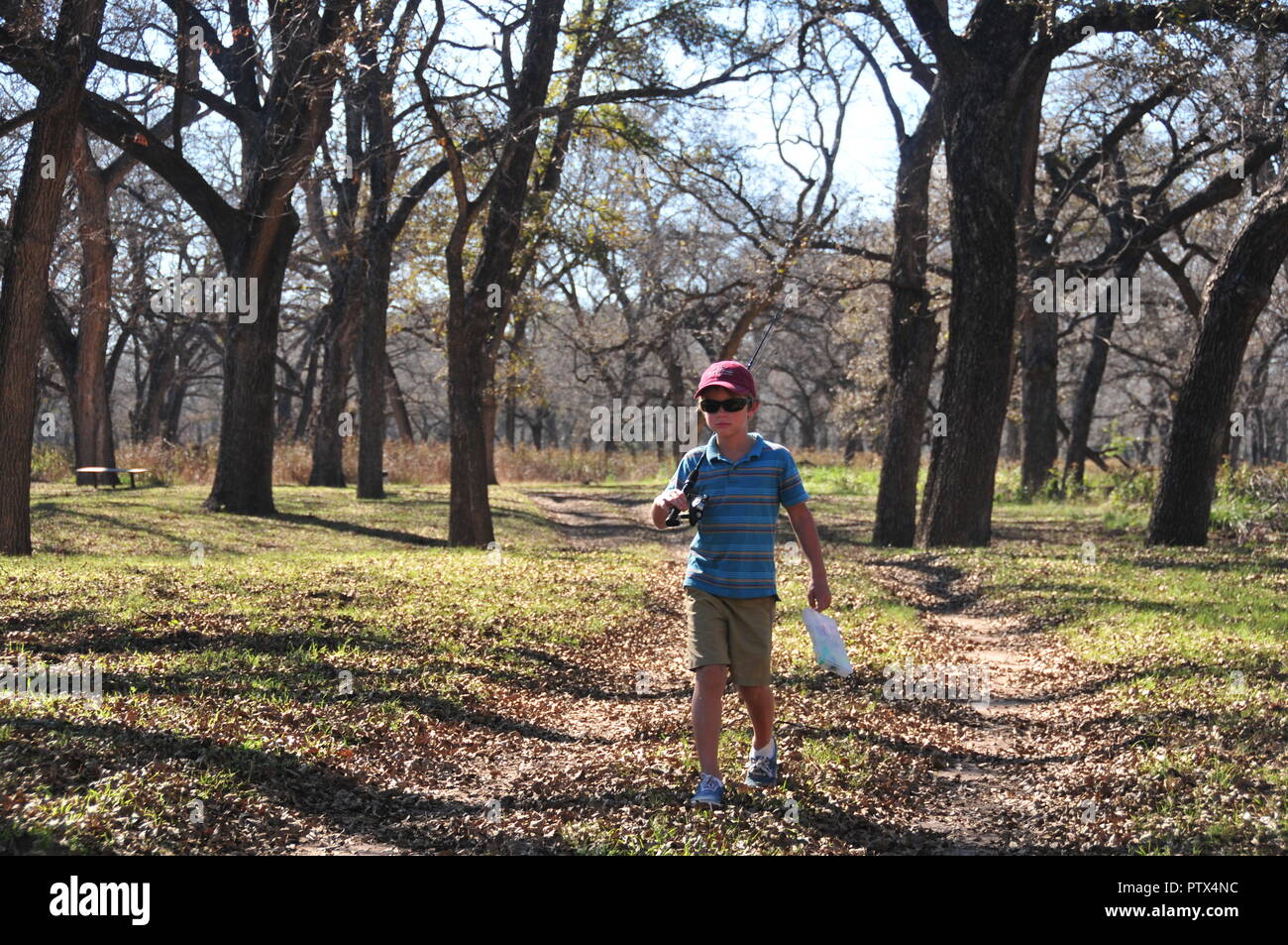 Boy walking on trail with fishing rod in autumn Stock Photo