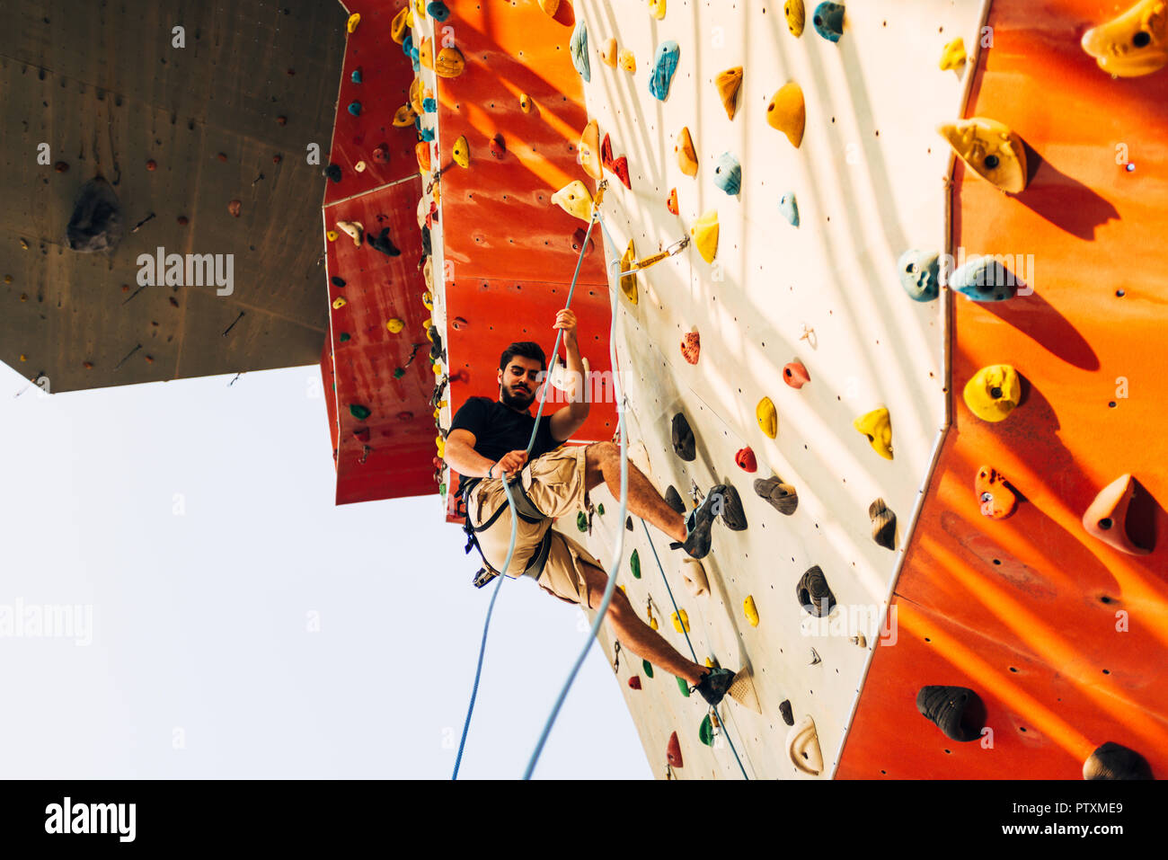 Man wearing belaying rope, climbing on a very high rock climbing wall ...
