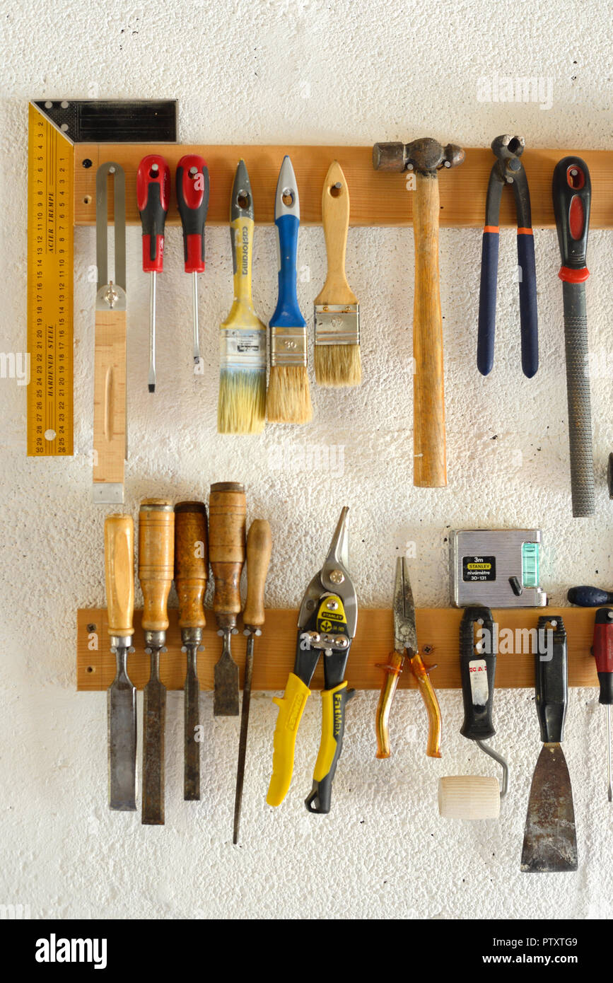 Woodworking Tools & Hand Tools including Paint Brushes, Chisels, Pliers and Hammers Hanging in Workshop or Garage Wall-Mounted Tool Rack Stock Photo