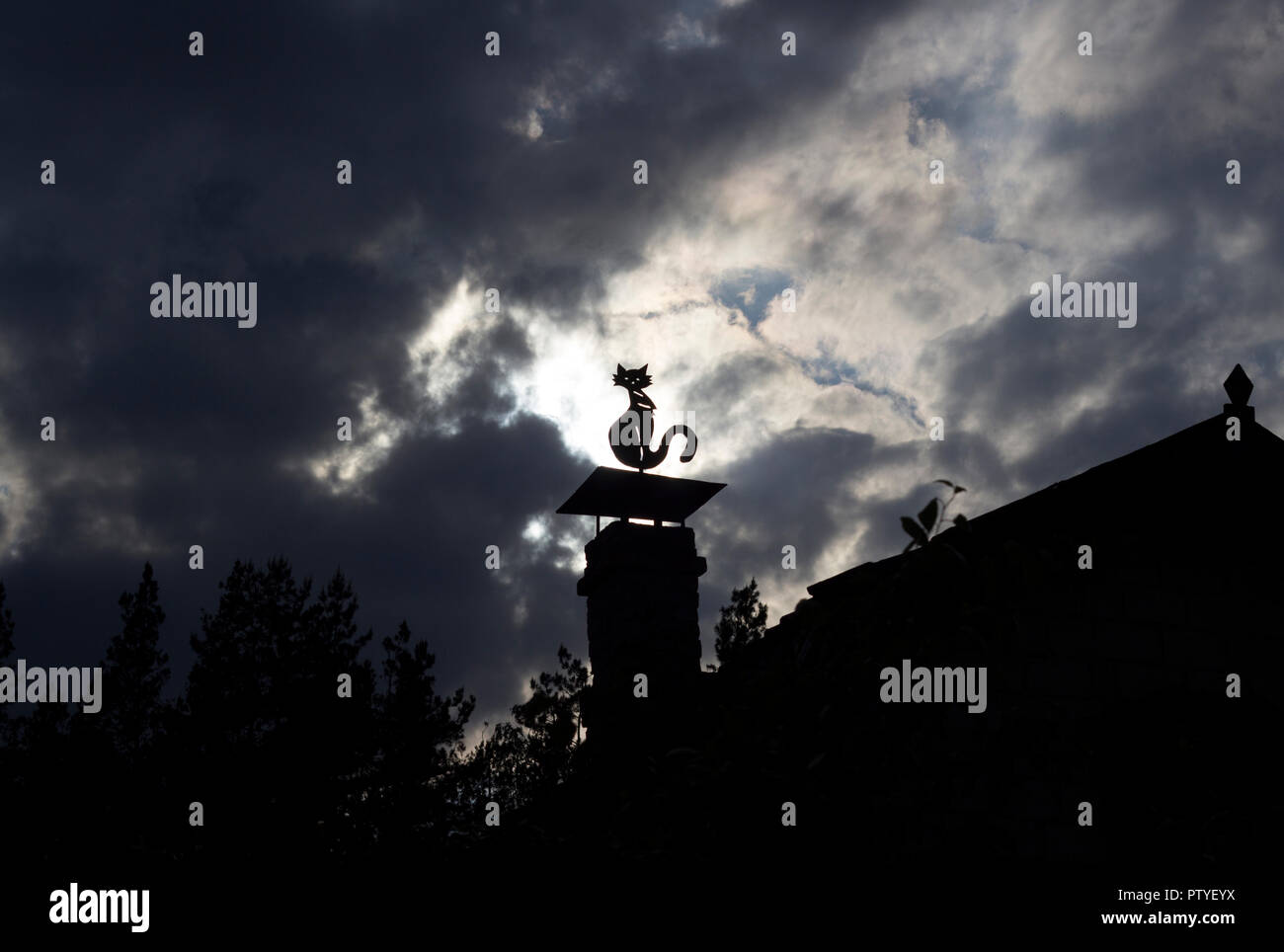A stuffed cat dummy sits on a chimney at home, thick black clouds and sun Stock Photo